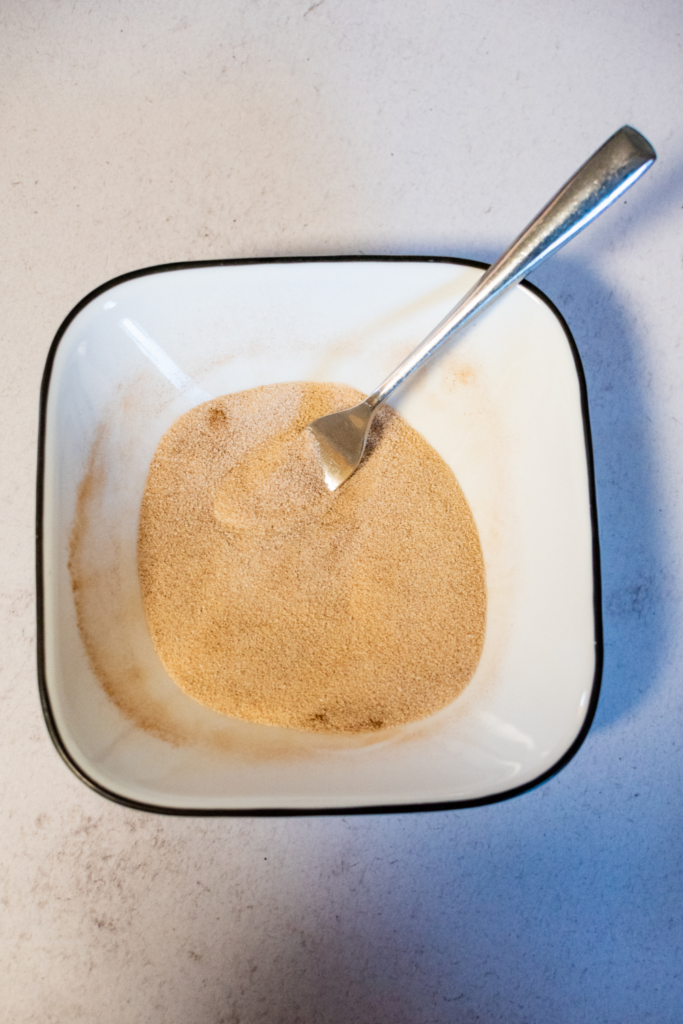 A white bowl of cinnamon and sugar mixed together with a spoon.