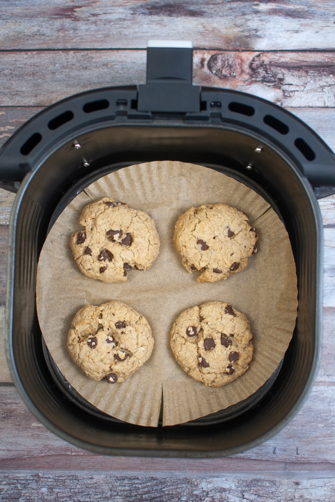 Cooked chocolate chip cookies on a parchment liner coming out of the air fryer