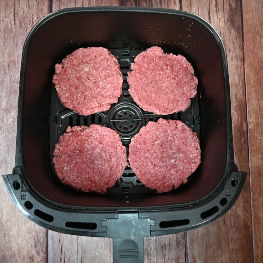 Four hamburger patties uncooked in an air fryer basket