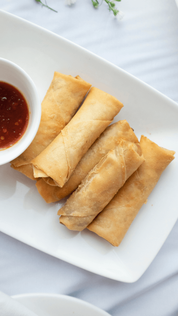 Five spring rolls with sauce on a white rectangular plate. 