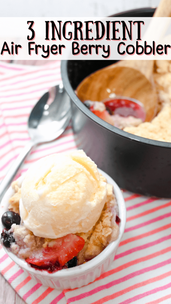 Close up image of this air fryer berry cobbler with a scoop of vanilla ice cream on top and the cake barrel full of the cobbler in the background all on a pink and orange striped towel 