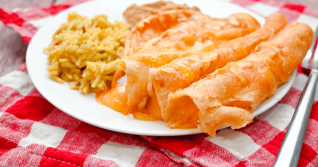 Air fryer cheese enchiladas on a white plate on a red checked towel with a fork and ready to eat. 