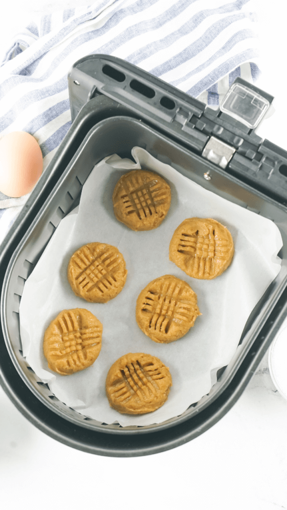 Six peanut butter cookies on parchment paper before cooking in the air fryer basket