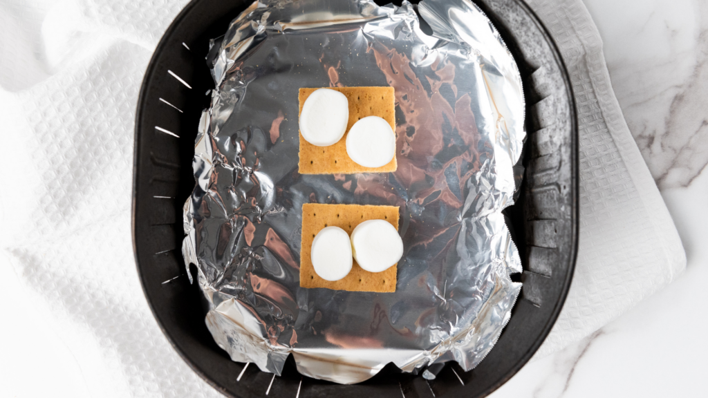 Putting the graham crackers and marshmallows on foil in the air fryer basket to make s'mores in the air fryer