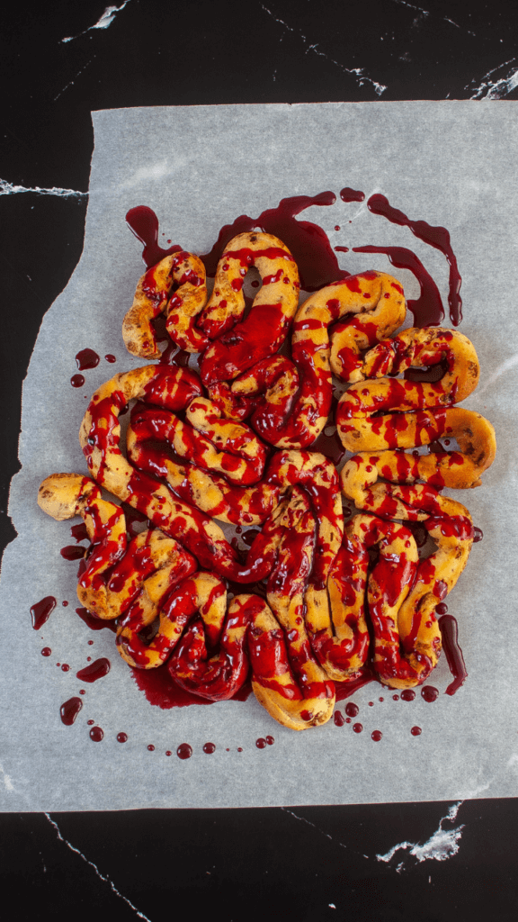 Parchment paper with the finished air fryer cinnamon roll intestines drizzled in red icing to look like blood