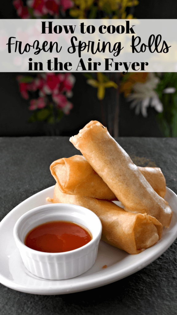 Three spring rolls on top of each other with sweet and sour sauce in a small ramekin all on a white oval plate. 
