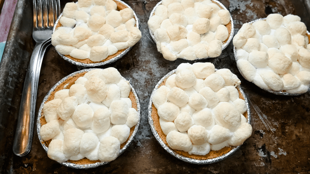 The finished mini s'mores pies topped with brown marshmallows on a cookie sheet with forks. 