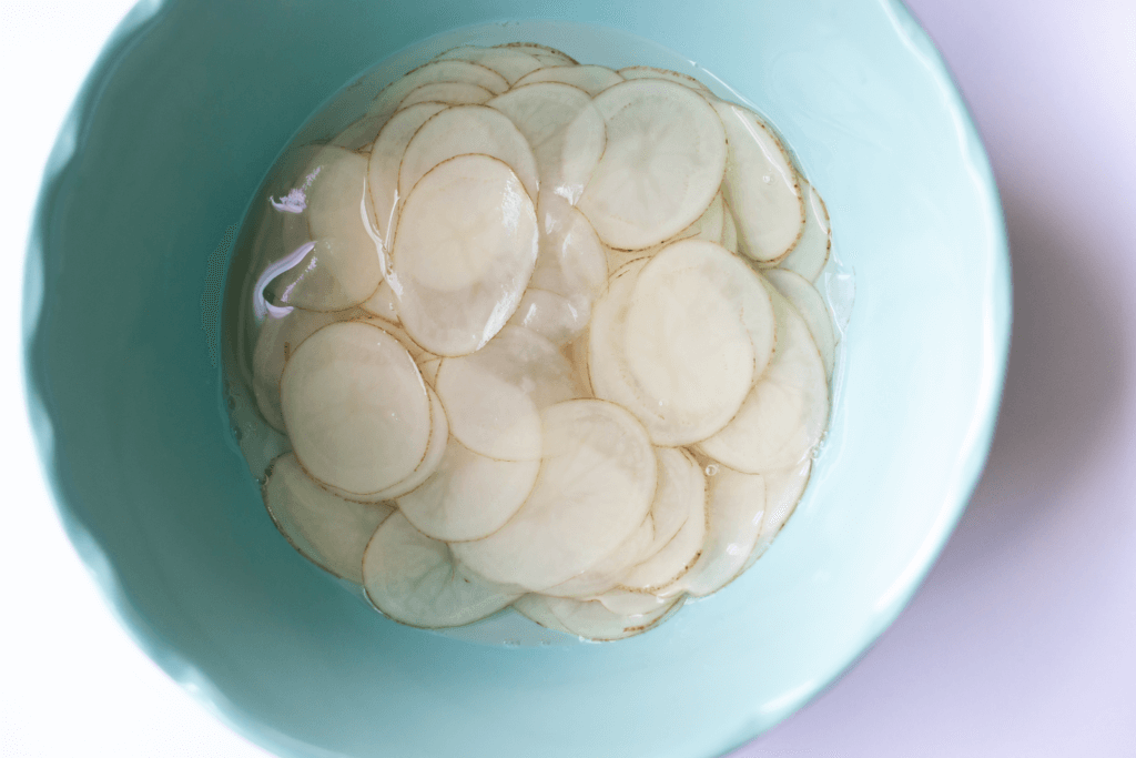Slices of potato in ice water in a blue bowl.