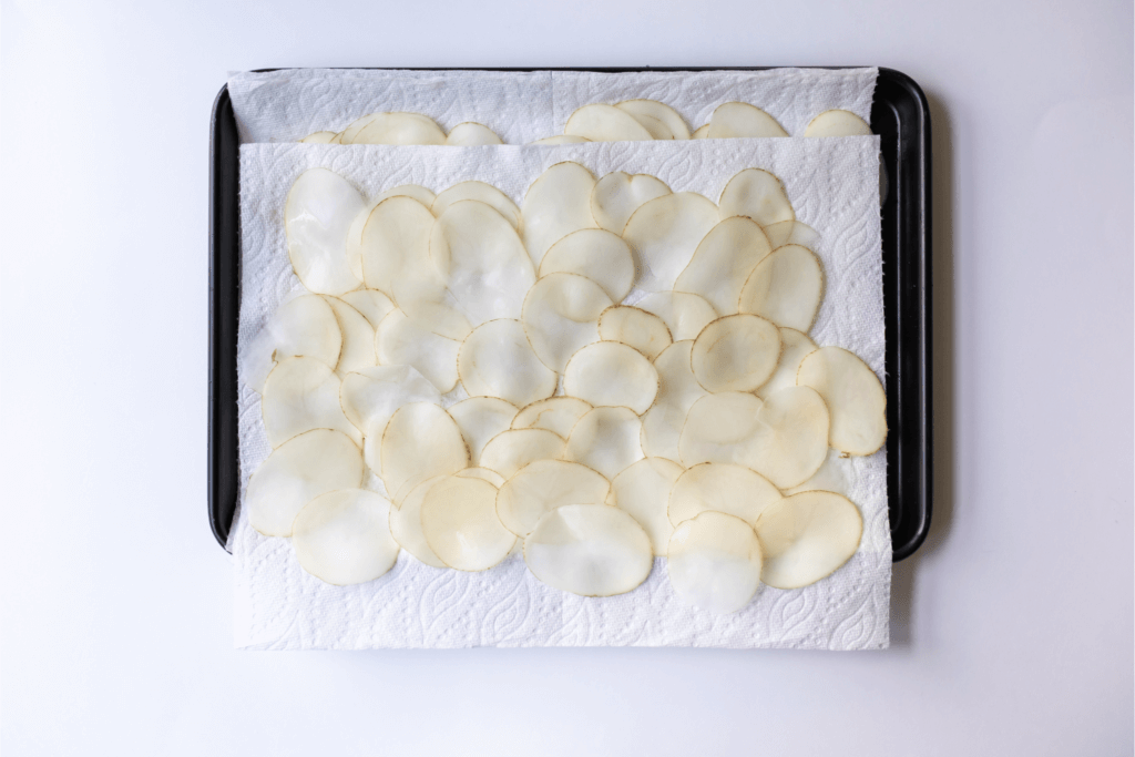 Slices of potato drying on a cookie sheet on paper towels.