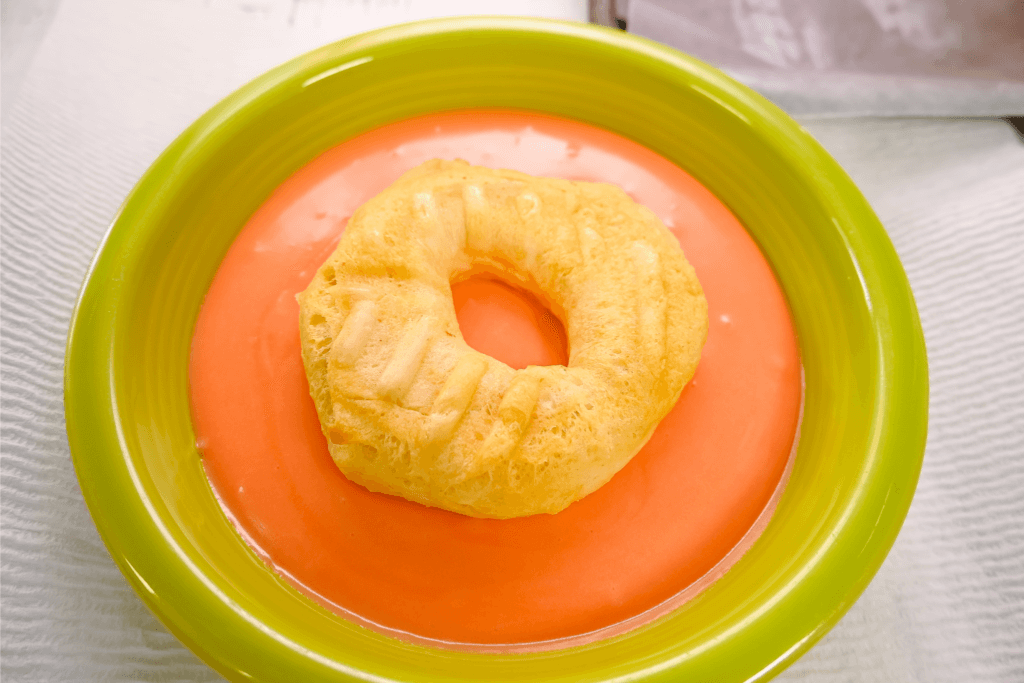 A green bowl with orange frosting and a biscuit donut in it. 