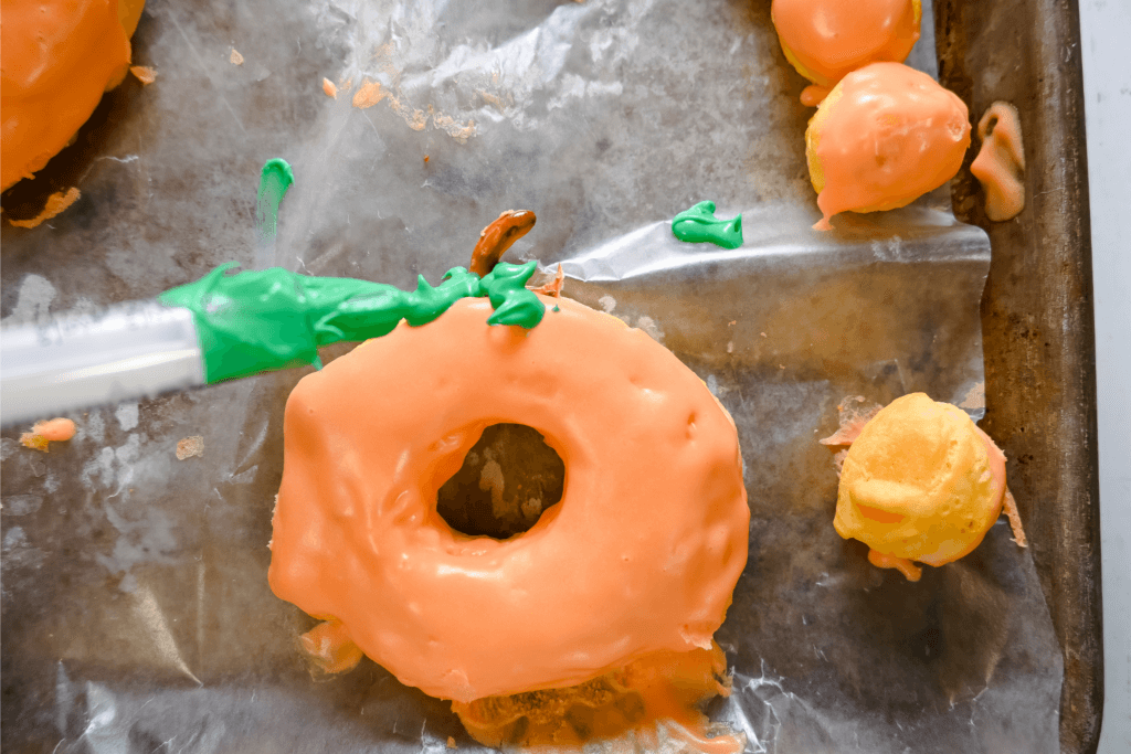 Using a medicine syringe to add green frosting to make leaves on the air fryer pumpkin donuts